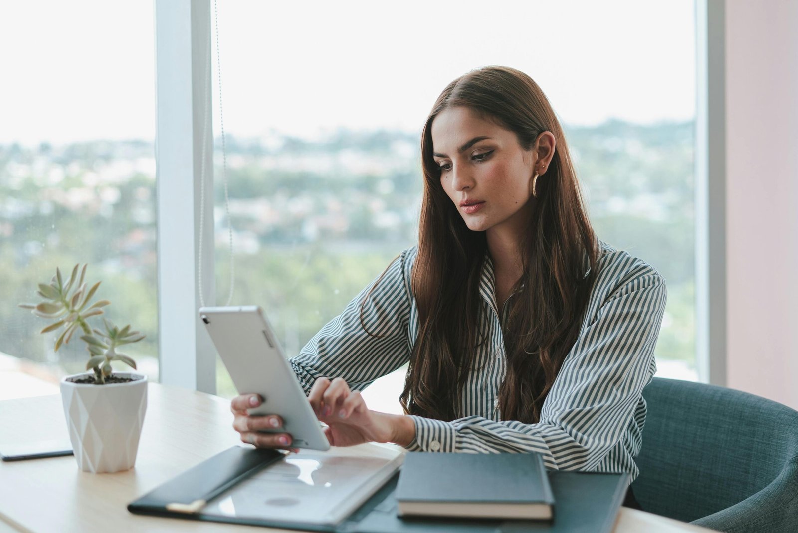 Confident businesswoman using a tablet while sitting at a desk in a modern office setting.