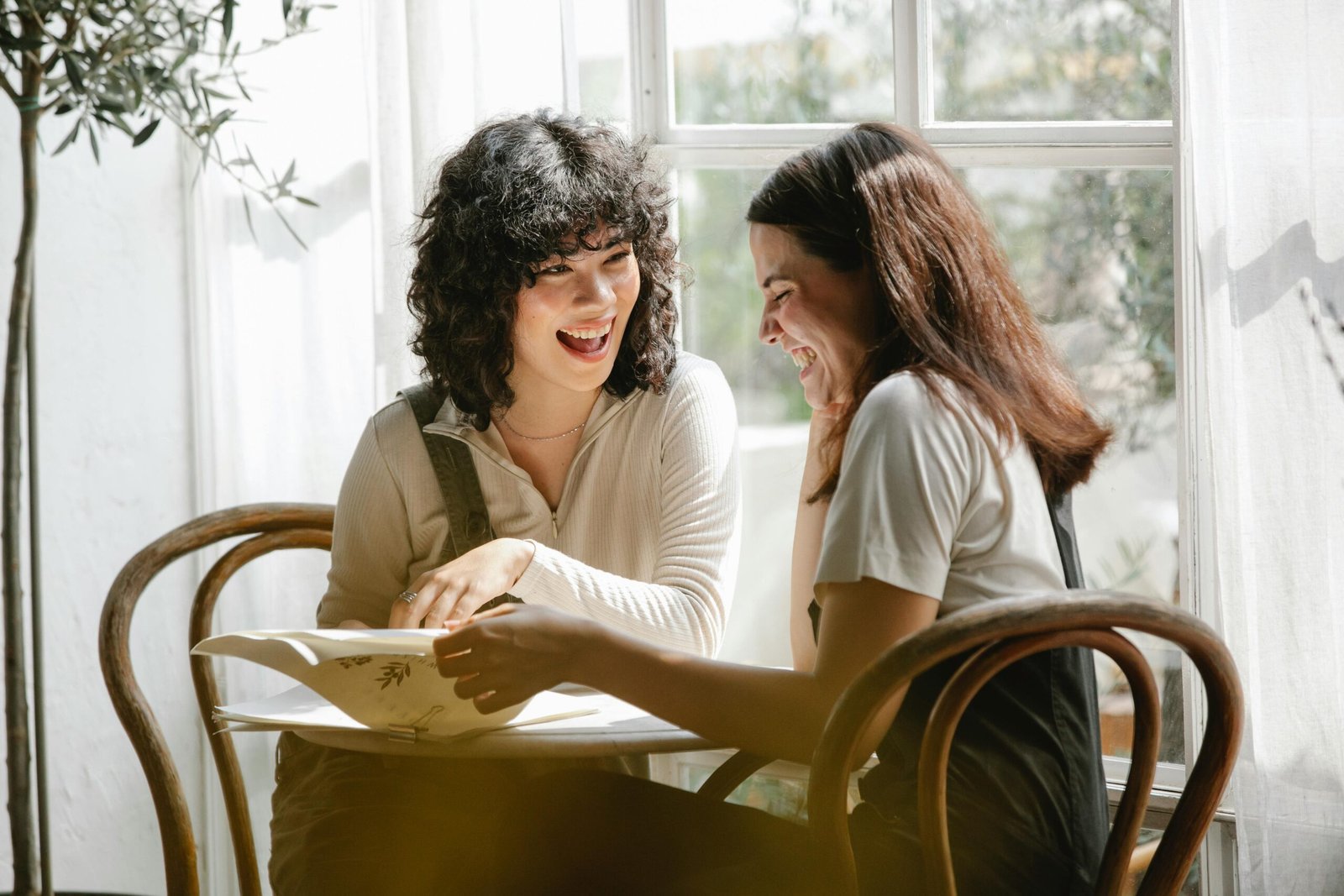 Laughing multiracial female colleagues wearing uniform flipping pages of papers while discussing work together