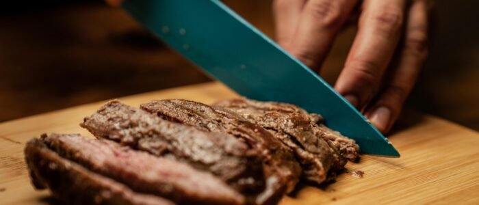 Hands slicing tender, juicy grilled steak on a wooden board, showcasing a mouth-watering culinary scene.